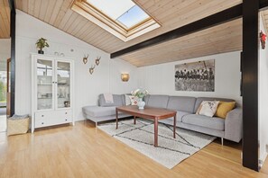 A modern living room with a wooden ceiling, a grey sofa, a white cabinet, and a large window. - Lovely bright cottage near Karrebæksminde (Karrebæksminde)