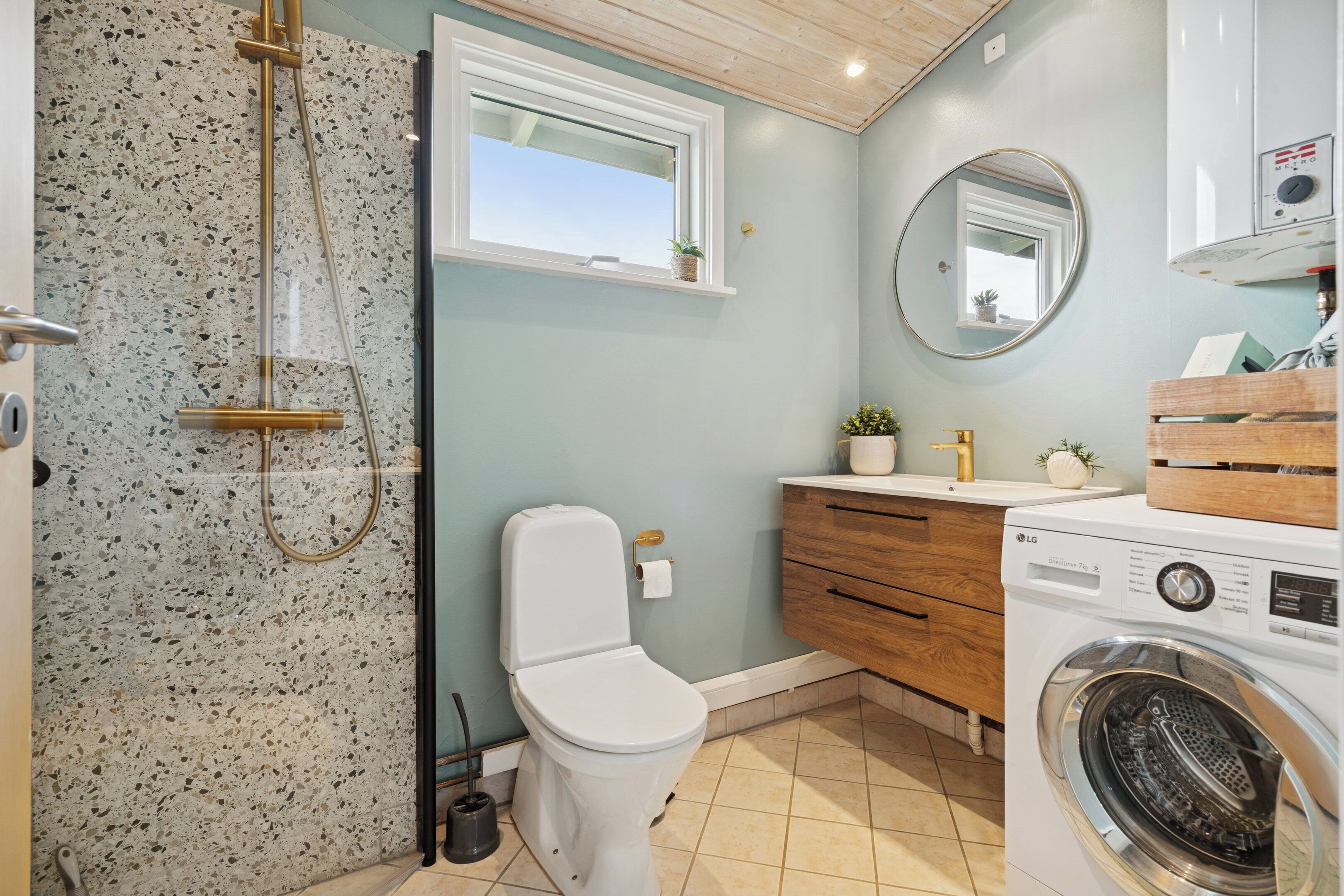 A bathroom with a shower, toilet, sink, and washing machine.
