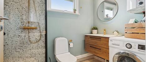 A bathroom with a shower, toilet, sink, and washing machine.