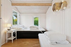 Ein Schlafzimmer mit Holzboden, einem Fenster, einem Nachttisch und einem Bett mit weißer Bettwäsche.
