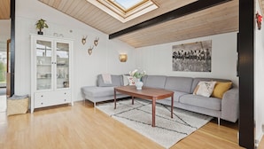 Un salon moderne avec un plafond en bois, un canapé gris, un meuble blanc et une grande fenêtre.