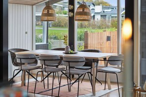 Un espace repas comprenant une table et des chaises, de grandes fenêtres et une vue sur l’extérieur.