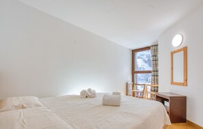A bedroom with a bed, a desk, a chair, and a window with curtains.