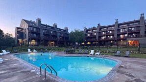 A swimming pool with lounge chairs and a building with balconies in the background. - Mountain Getaway | Pool, Hot Tub + Fall Hiking (Lutsen)