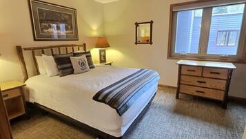 A bedroom with a bed, bedside table, lamp, dresser, and a window.