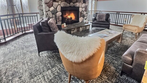 A cozy living room with a stone fireplace, comfortable seating, and a balcony railing. - Mountain Getaway | Pool, Hot Tub + Fall Hiking (Lutsen)