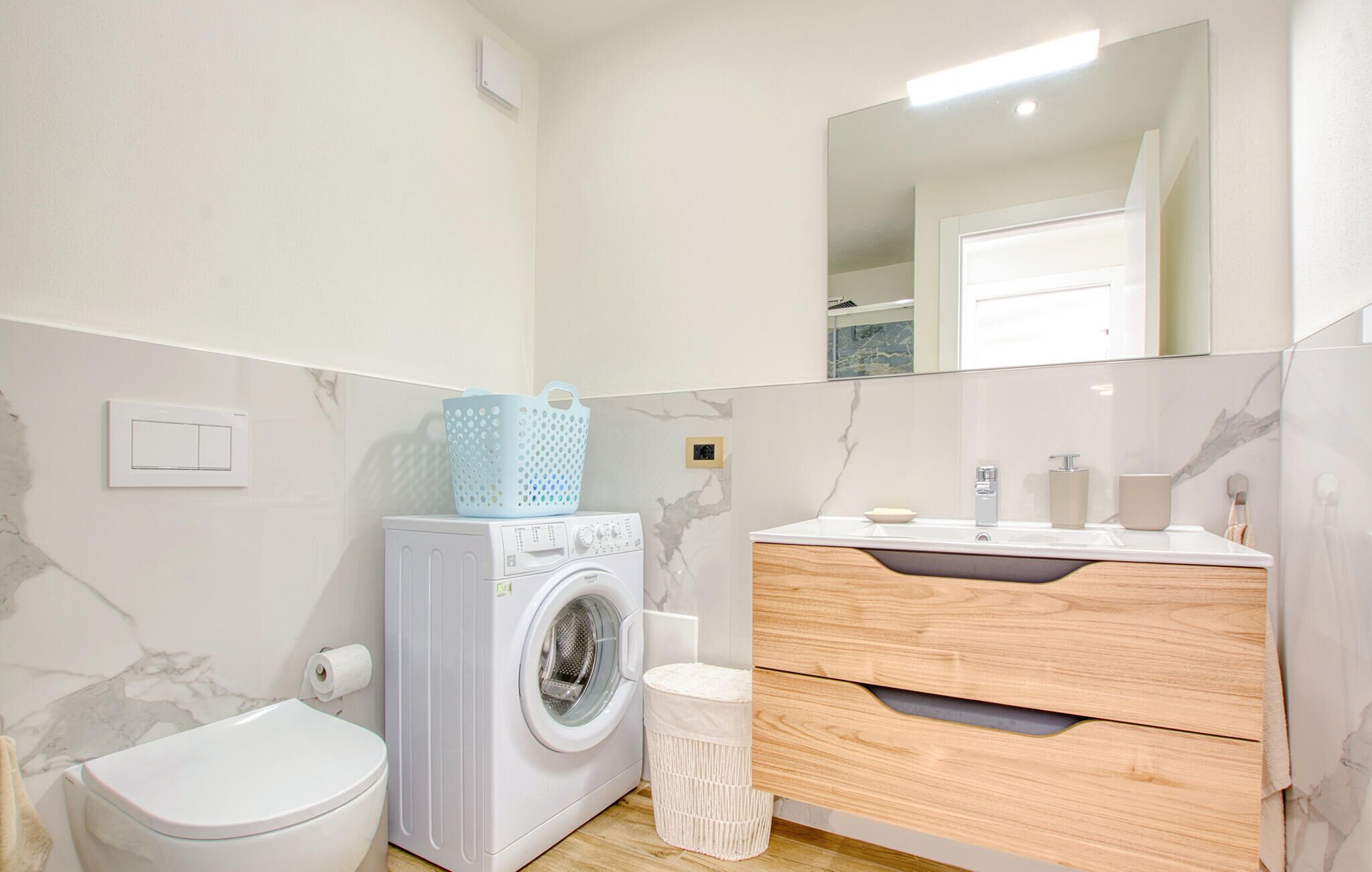 Un baño moderno con lavadora, inodoro, tocador con espejo y paredes de mármol.