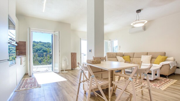 A spacious living area with a large table, wooden chairs, a sofa, and a balcony with a view of the forest. - 1 bedroom lovely apartment in Recco (Recco)