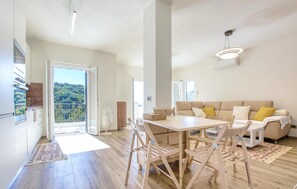 A spacious living area with a large table, wooden chairs, a sofa, and a balcony with a view of the forest. - 1 bedroom lovely apartment in Recco (Recco)