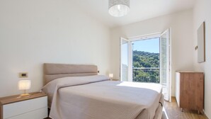 A bedroom with a bed, bedside tables, a nightstand, a lamp, a wooden cabinet, and a balcony with a view of trees and hills. - 1 bedroom lovely apartment in Recco (Recco)