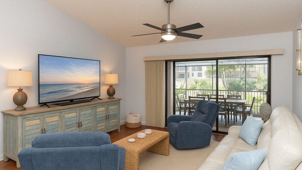 Ein Wohnzimmer mit Fernseher, zwei Sesseln, einer Couch, einem Couchtisch und einem Balkon mit Aussicht.