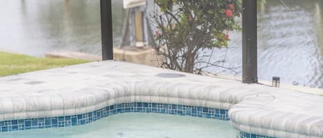 A hot tub with a tiled edge, a view of a body of water, and a tree with pink flowers.