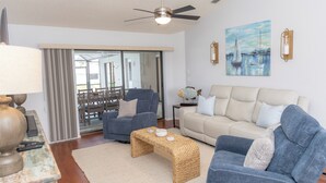Ein Wohnzimmer mit Deckenventilator, einer Couch, einem Sessel, einem Couchtisch und einem Bild an der Wand.