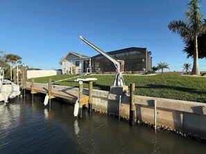 Un port esportiu amb un vaixell amarrat, una passera de formigó i una casa moderna amb un gran finestral de vidre.