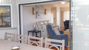 Ein modernes Wohnzimmer mit einer Couch, Sesseln und einer Glastür zu einem anderen Raum.