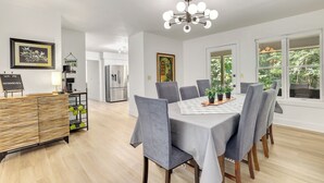 A modern dining area with a table set for six, surrounded by grey upholstered chairs. A chandelier hangs above, and there is a view of a kitchen and a dining area in the background. - Close to Trails+3BR Retreat+Sleeps 10+Bunk Room (Bella Vista)