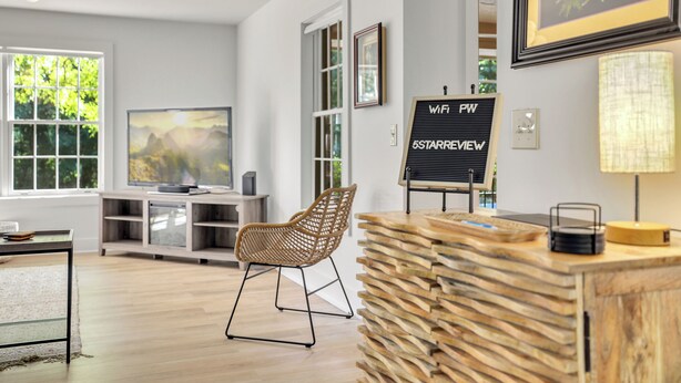 A modern living room with a wooden coffee table, a wicker chair, a TV, and a sign indicating WiFi and 5G availability. - Close to Trails+3BR Retreat+Sleeps 10+Bunk Room (Bella Vista)