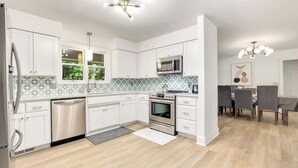 A modern kitchen with white cabinets, stainless steel appliances, and a dining area with a table and chairs. - Close to Trails+3BR Retreat+Sleeps 10+Bunk Room (Bella Vista)
