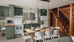 Une cuisine avec des meubles de couleur verte, une table à manger en bois, des chaises blanches et un escalier en bois.