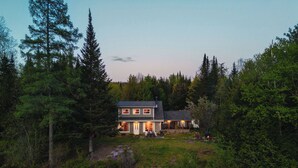 Une maison à deux étages avec une jetée qui s’avance sur une étendue d’eau calme, le tout entouré d’une forêt dense.