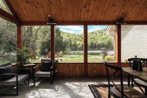 A covered patio with wooden beams, outdoor furniture, and a view of a lake and forest. - Lakeside cottage | family | Canoe, Kayak | Veranda (Labelle)