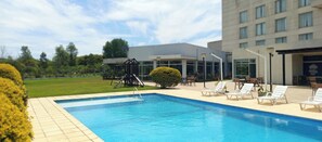 Une piscine avec des chaises longues, un espace de jeux pour enfants et un bâtiment doté de grandes fenêtres.
