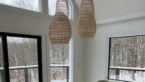 Un espace repas moderne avec une grande table, six chaises et deux lustres suspendus en osier.