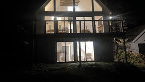 Une maison moderne à deux étages, dotée de grandes fenêtres et d’un balcon.