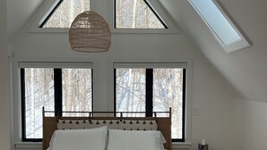 Une chambre avec un grand lit, deux fenêtres, un puits de lumière et une table de chevet.
