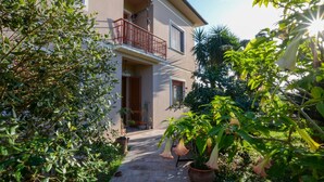Ein zweistöckiges Gebäude mit Balkon, umgeben von üppiger Vegetation und Blumentöpfen.