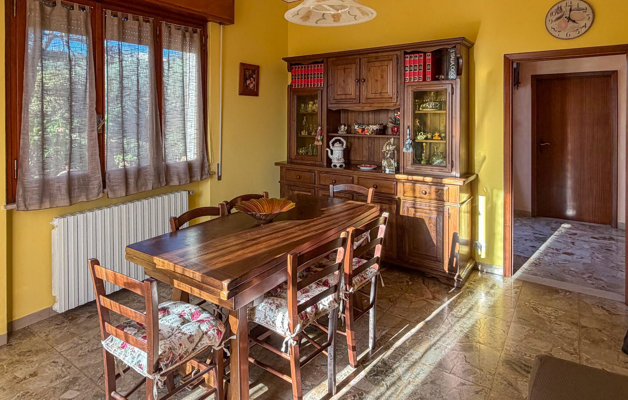 Un coin repas avec une table et des chaises en bois, un buffet avec des portes en verre et une horloge au mur.