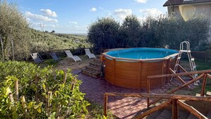 Ein hölzerner Pool mit einer Leiter, umgeben von einer Ziegelterrasse und Liegestühlen.