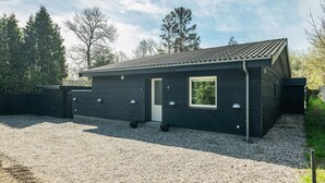 Moderni, kaksikerroksinen talo, jossa on tumma julkisivu, tiilikatto ja sorapäällysteinen ajotie.