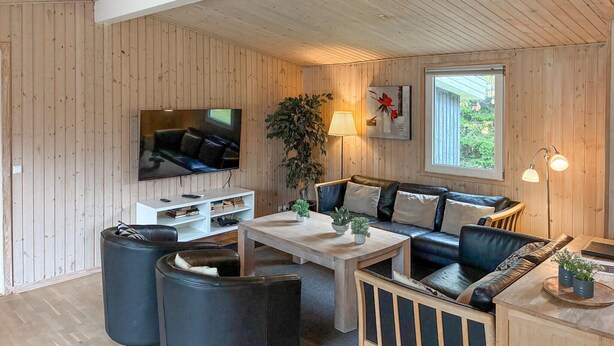 Una sala de estar acogedora con televisor, sofá y mesa de centro, con paredes de madera y un ventanal grande.