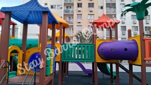 Un parque infantil con diversas estructuras de juego, incluyendo toboganes y zonas de escalada, con edificios residenciales de fondo.