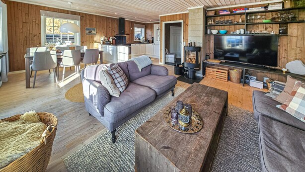 A cozy living room with a sofa, coffee table, and a TV. There's a dining area with chairs and a table. The room has wooden walls and a large window. - Nice home in Rauland with WiFi (Rauland)