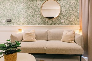 A beige sofa with patterned cushions, a round mirror on the wall, and a potted plant on a round table. - Villa Iris- Private Pool retreat in Las Iguanas Golf Residence, Cap Cana (Punta Cana)