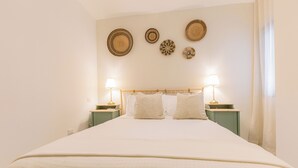 Una cama bien hecha con cabecera de madera, dos lámparas de noche y cuatro adornos de pared.