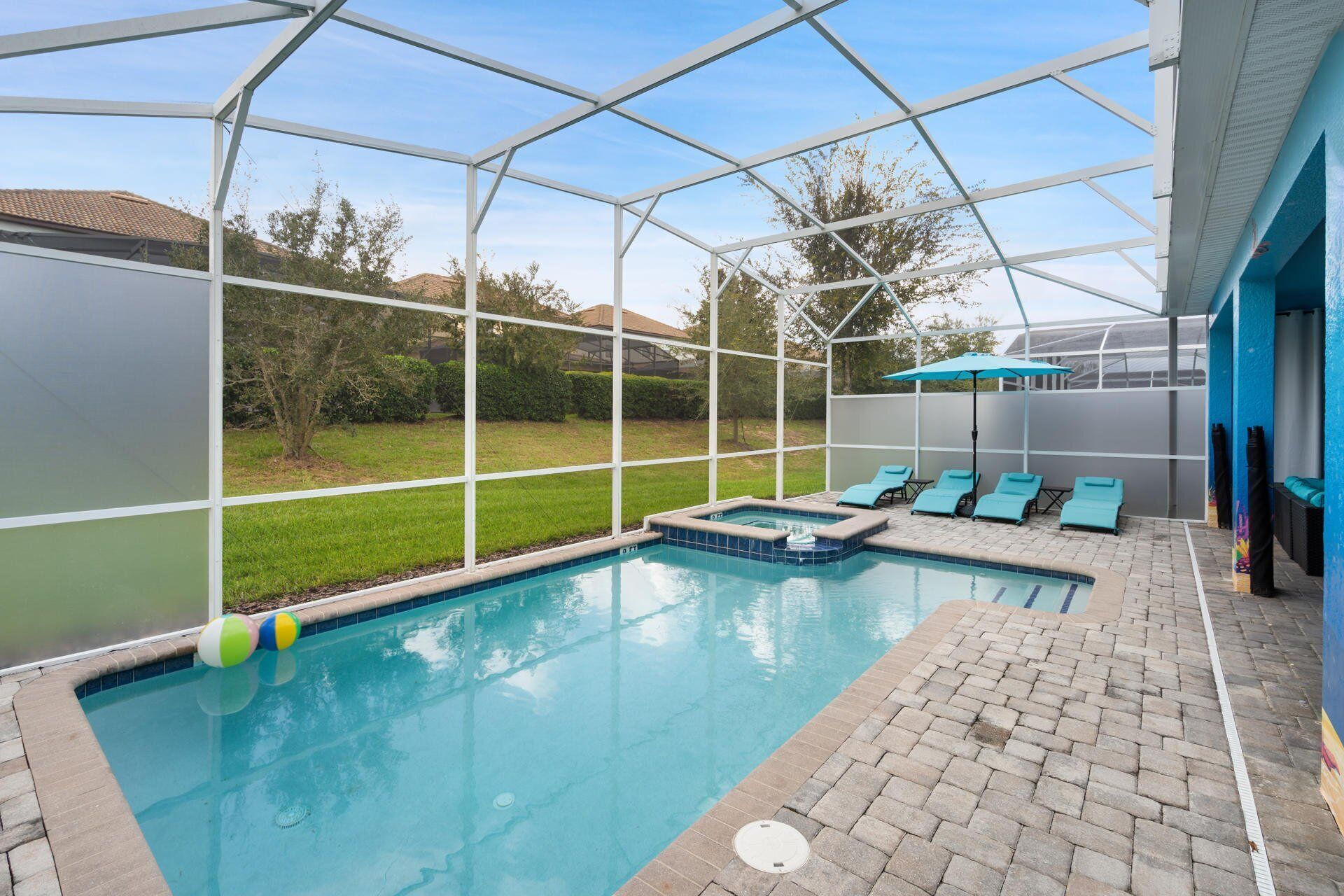 A swimming pool with a glass enclosure, lounge chairs, and a small hot tub area.