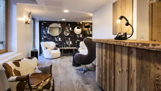 A modern interior with a wooden reception desk, two armchairs, a round mirror, and a wall with a distressed black and white pattern. - 2-room Apartment for 4 People (Les Deux Alpes)