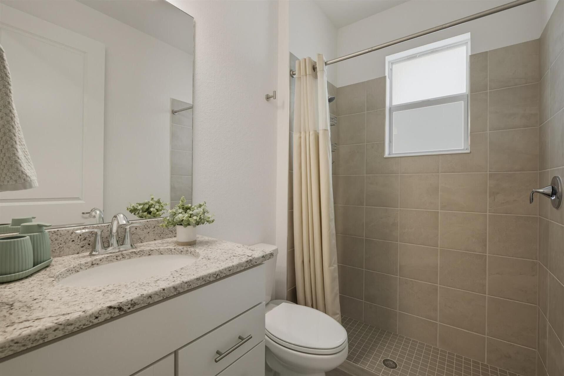 A bathroom with a shower, toilet, sink, and a mirror.