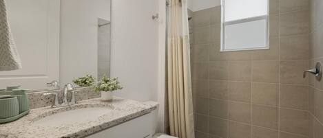 A bathroom with a shower, toilet, sink, and a mirror.