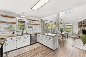 A modern kitchen with white cabinets, a granite countertop, and a dining area with a stone fireplace. - 3 Kings! Hot Tub/Pool-Fire Pit-GameRm GYM+ PickleB (Canyon Lake)