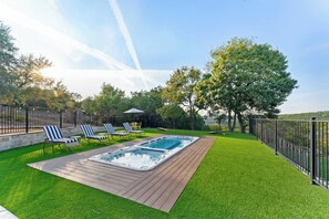 Un jardin avec un jacuzzi, du gazon synthétique et une terrasse en bois.