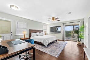 Une chambre à coucher comprenant un lit, un bureau, une chaise, un ventilateur de plafond et une vue sur l’extérieur, accessible par une porte-fenêtre coulissante.