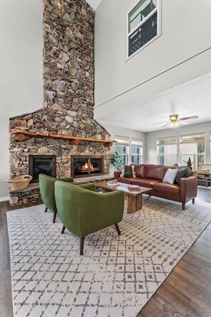 A living room with a stone fireplace, green armchairs, a brown sofa, and a patterned rug. - 3 Kings! Hot Tub/Pool-Fire Pit-GameRm GYM+ PickleB (Canyon Lake)