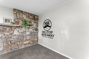 A room with a stone wall, a logo for Hilltop Hideaway, and a framed picture on the wall. - 3 Kings! Hot Tub/Pool-Fire Pit-GameRm GYM+ PickleB (Canyon Lake)