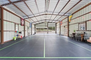 A covered sports court with a net, seating area, and storage racks. - 3 Kings! Hot Tub/Pool-Fire Pit-GameRm GYM+ PickleB (Canyon Lake)
