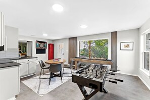 A modern kitchen with a dining area, a foosball table, and a window with a view of trees. - 3 Kings! Hot Tub/Pool-Fire Pit-GameRm GYM+ PickleB (Canyon Lake)