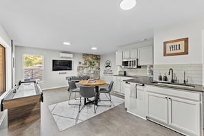 A modern kitchen with white cabinetry, a stone accent wall, and a dining area with a round table and chairs. - 3 Kings! Hot Tub/Pool-Fire Pit-GameRm GYM+ PickleB (Canyon Lake)
